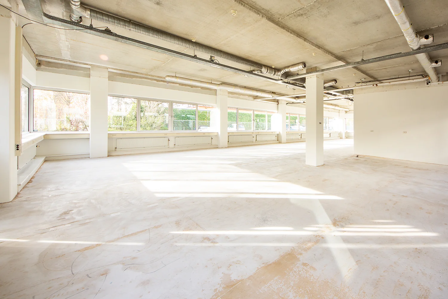 Lichte, lege kantoorruimte aan de Huis ter Heideweg met grote ramen en een betonnen plafond.